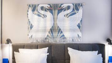 Una cama con dos almohadas blancas y un tapiz de pared con cisnes blancos.