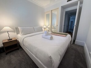 A neatly made bed with a rolled towel, a bedside lamp, and a nightstand. - Manly Beachfront 3BR, walk to cafes & dining (Manly)
