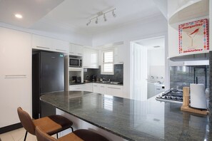 A modern kitchen with a central island, stainless steel appliances, and a view to the dining area. - Manly Beachfront 3BR, walk to cafes & dining (Manly)