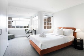Ein modernes Hotelzimmer mit einem großen Bett, einem Schreibtisch und Blick auf die Stadt durch die Fenster.