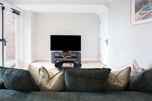 Ein Wohnzimmer mit einer schwarzen Unterhaltungsecke, einem Flachbildfernseher und einer Couch mit Kissen.