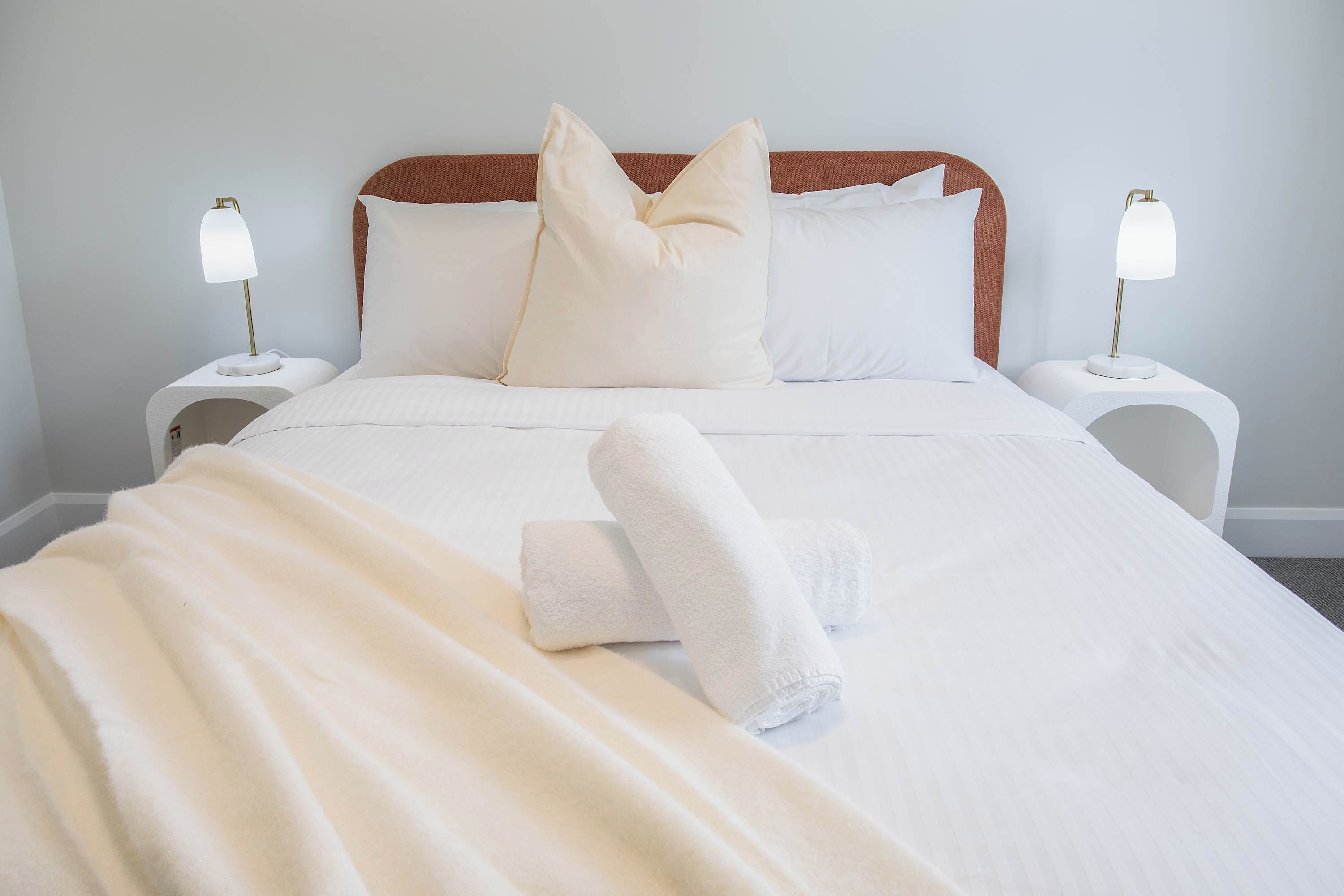 A neatly made bed with white linens, two bedside lamps, and two pillows.