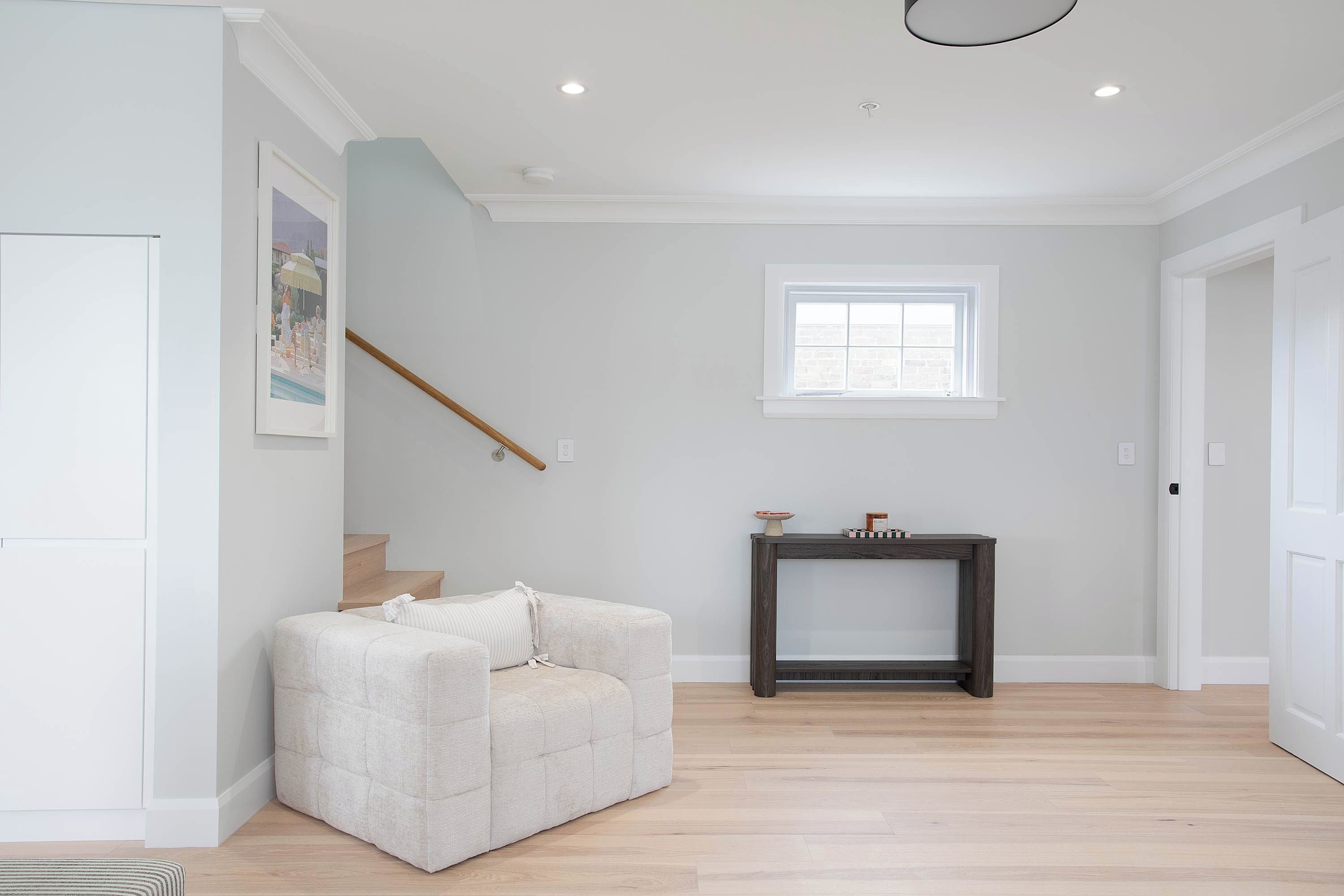 A spacious room with a light-colored sofa, a small table with decorative items, a window, and a staircase.