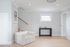 Ein geräumiges Zimmer mit einem hellen Sofa, einem kleinen Tisch mit Dekoration und einem Fenster sowie einer Treppe.