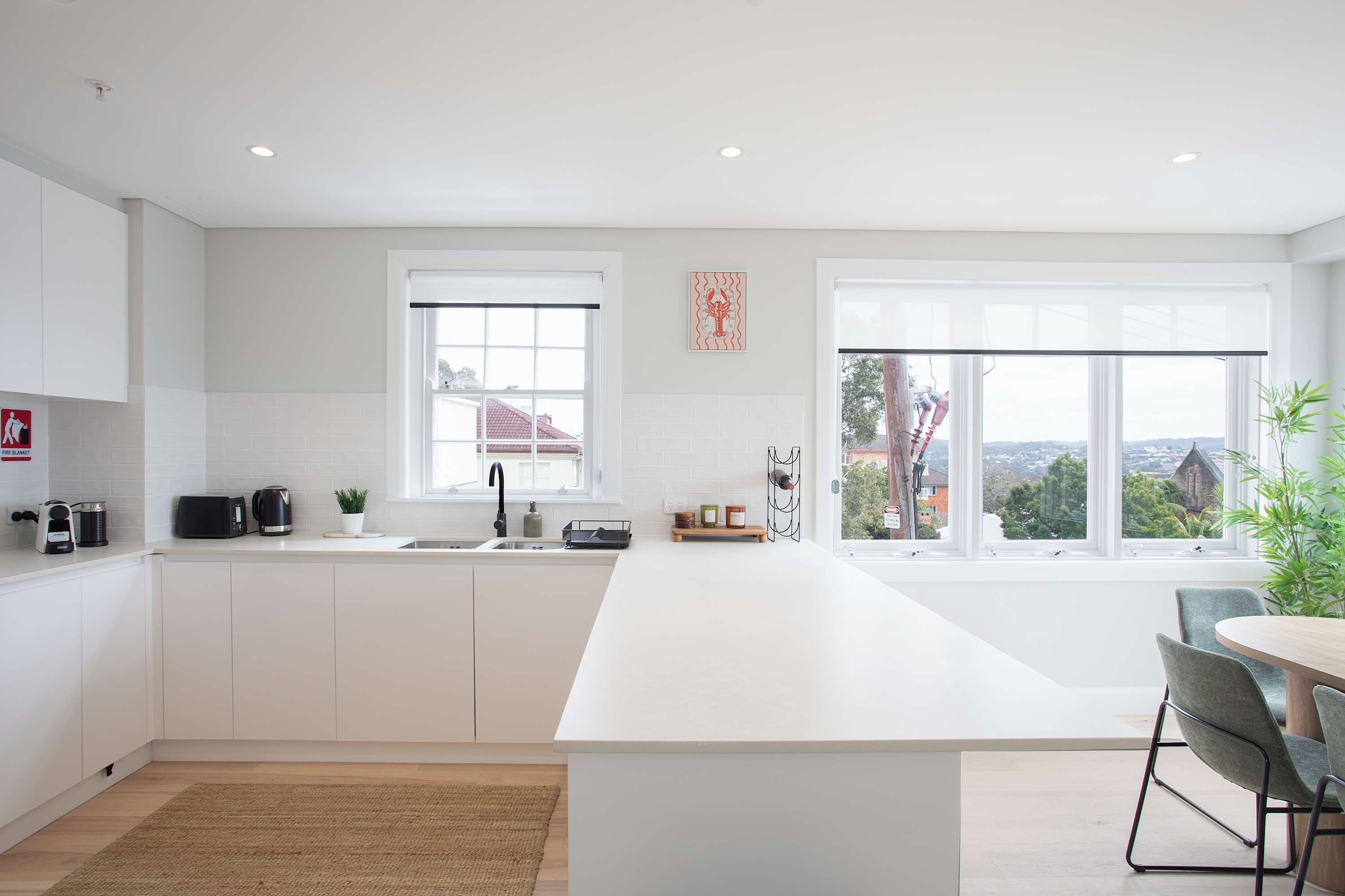 A modern kitchen with a large island, white cabinetry, a window with a view, and a dining area with a table and chairs.