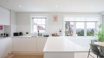 A modern kitchen with a large island, white cabinetry, a window with a view, and a dining area with a table and chairs.