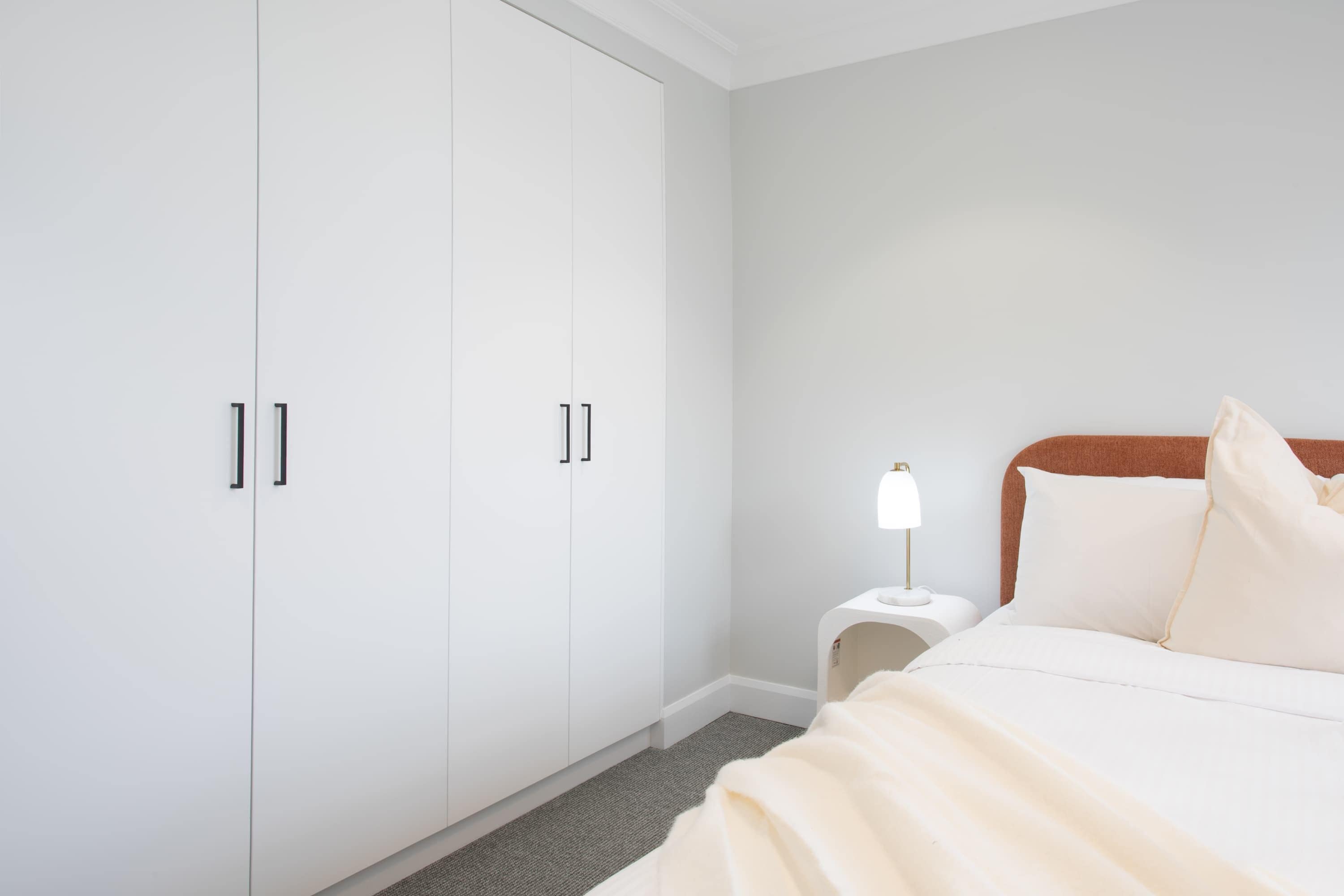 A bedroom with a bed, a nightstand, a lamp, and a wardrobe.