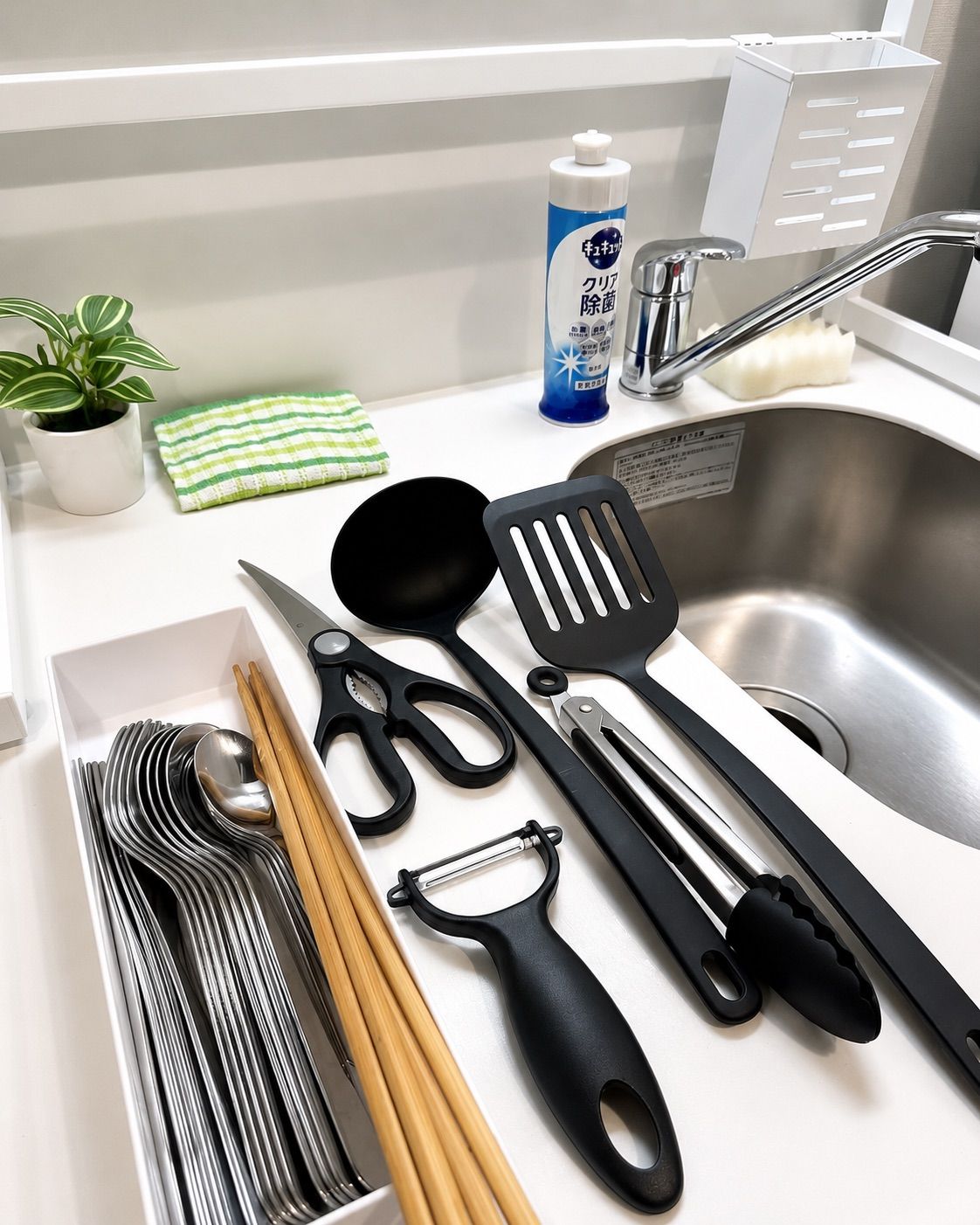 A kitchen counter with various utensils, a plant, a cleaning product, and a sink.