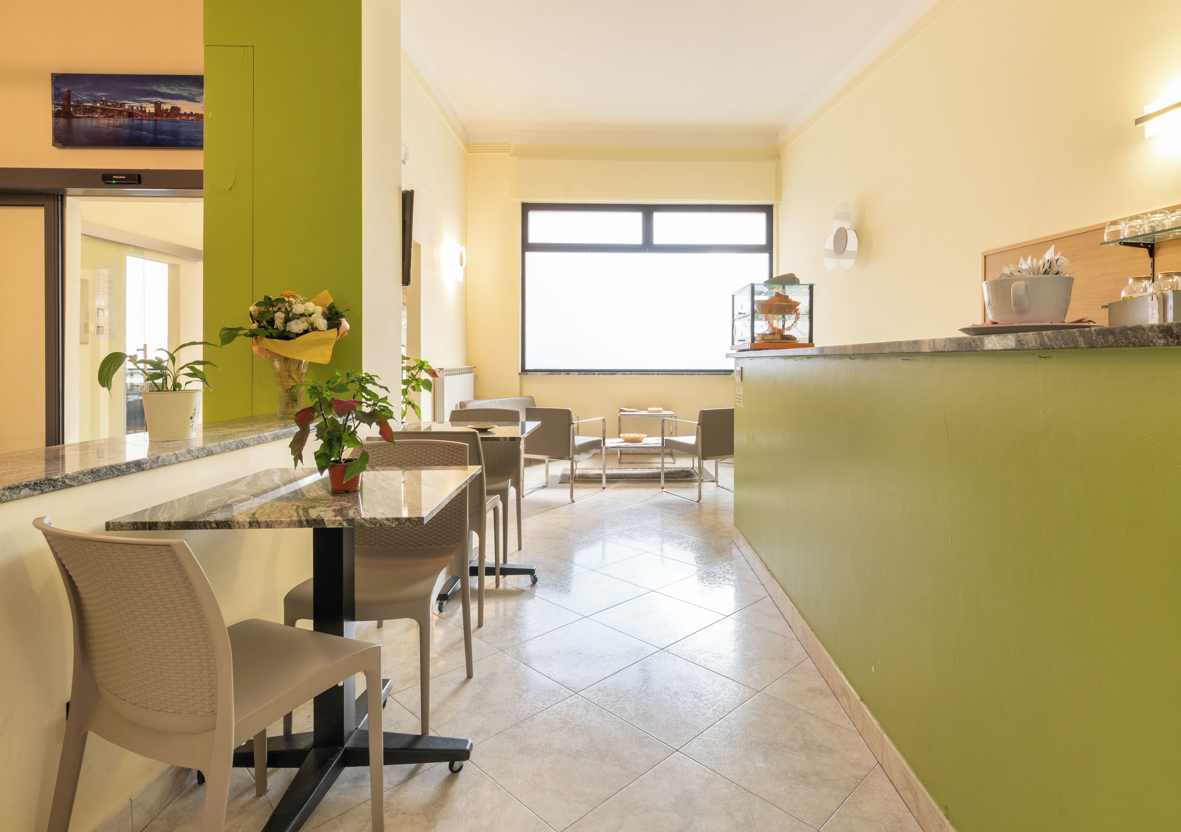 Una cucina moderna con zona pranzo, caratterizzata da un piano di lavoro in granito, sedie, una pianta in vaso e un'ampia finestra.