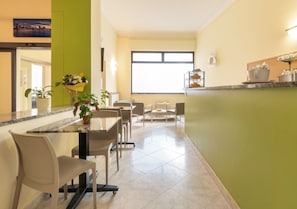 A modern kitchen with a dining area, featuring a granite countertop, chairs, a potted plant, and a large window.