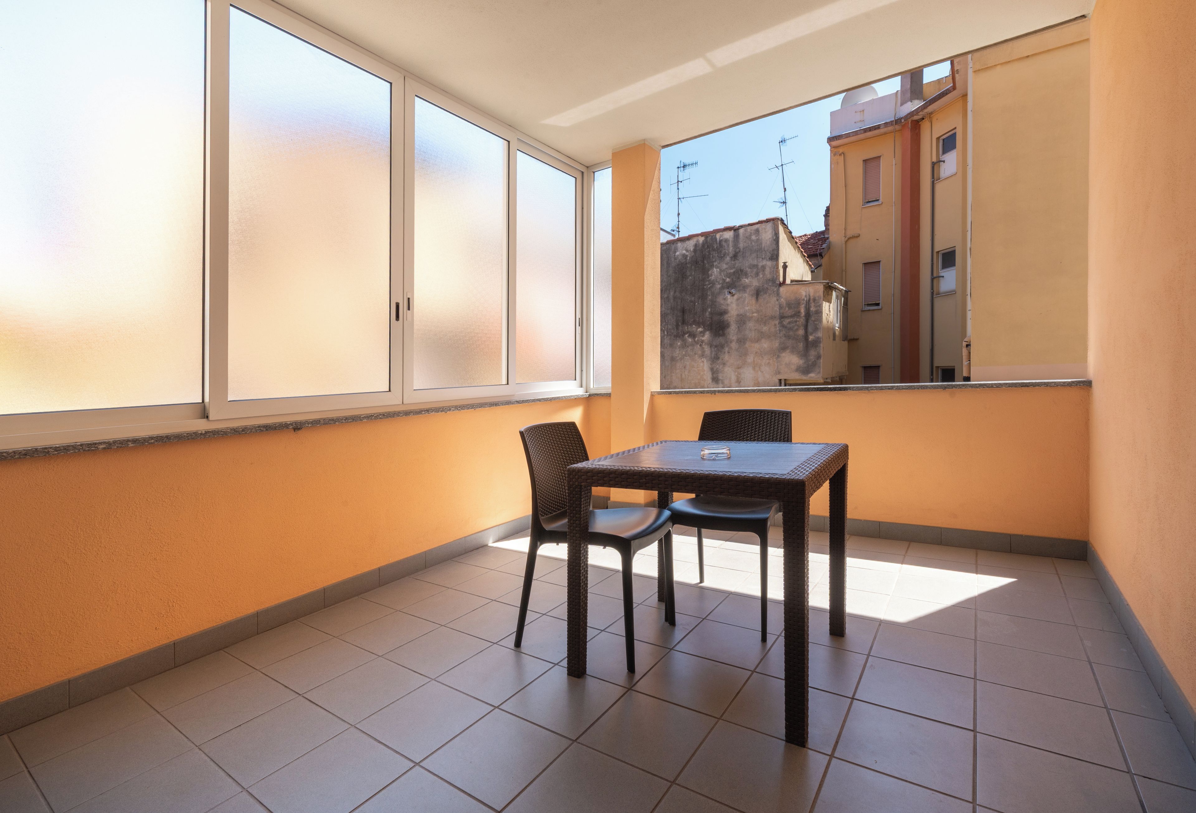 Un piccolo balcone con tavolo e sedie, ampie finestre e vista sugli edifici.