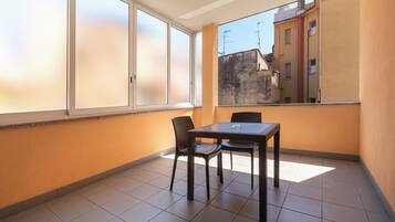 Un piccolo balcone con tavolo e sedie, ampie finestre e vista sugli edifici.