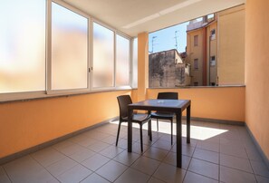 A small balcony with a table and chairs, large windows, and a view of buildings.