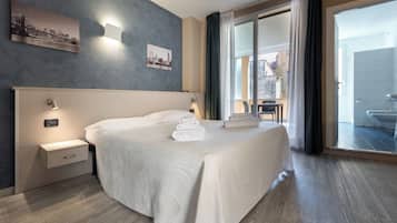 Hotellihuone, jossa on suuri sänky, yöpöytä, seinään kiinnitetty lamppu, kehystetty taulu ja näkymä ulkopuolella olevalle parvekkeelle.