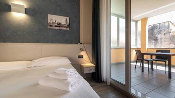 Una camera d'hotel con un letto, un comodino con una lampada, un quadro al muro e vista sul balcone esterno.