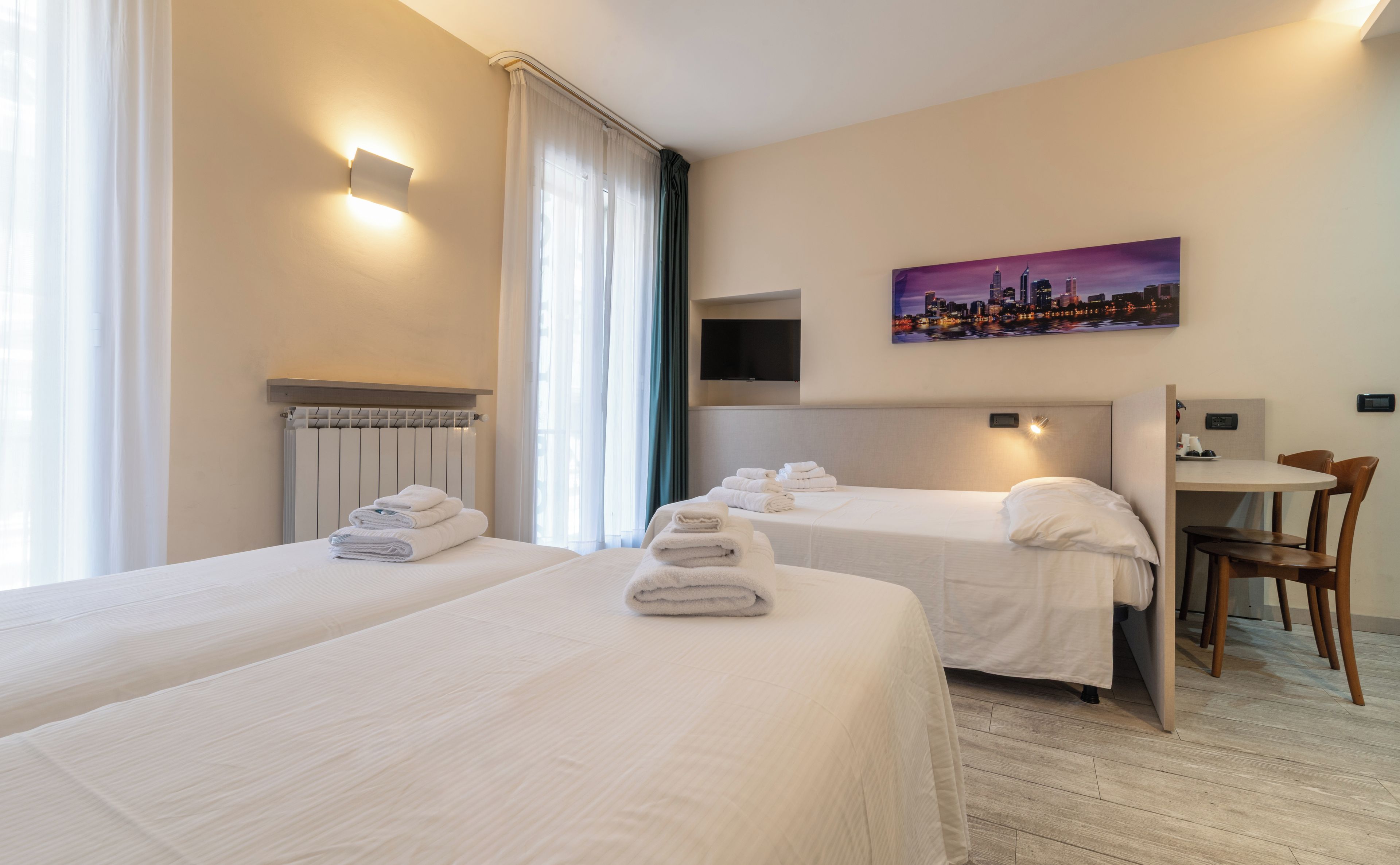 Une chambre d’hôtel avec deux lits, un téléviseur à écran plat, un tableau représentant un paysage urbain et un bureau avec une chaise.