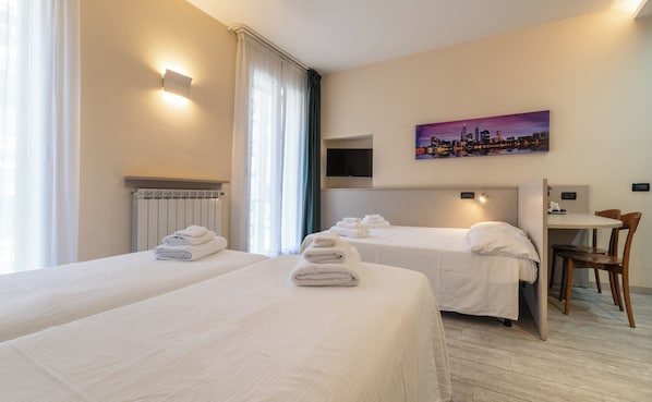 Une chambre d’hôtel avec deux lits, un téléviseur à écran plat, un tableau représentant un paysage urbain et un bureau avec une chaise.