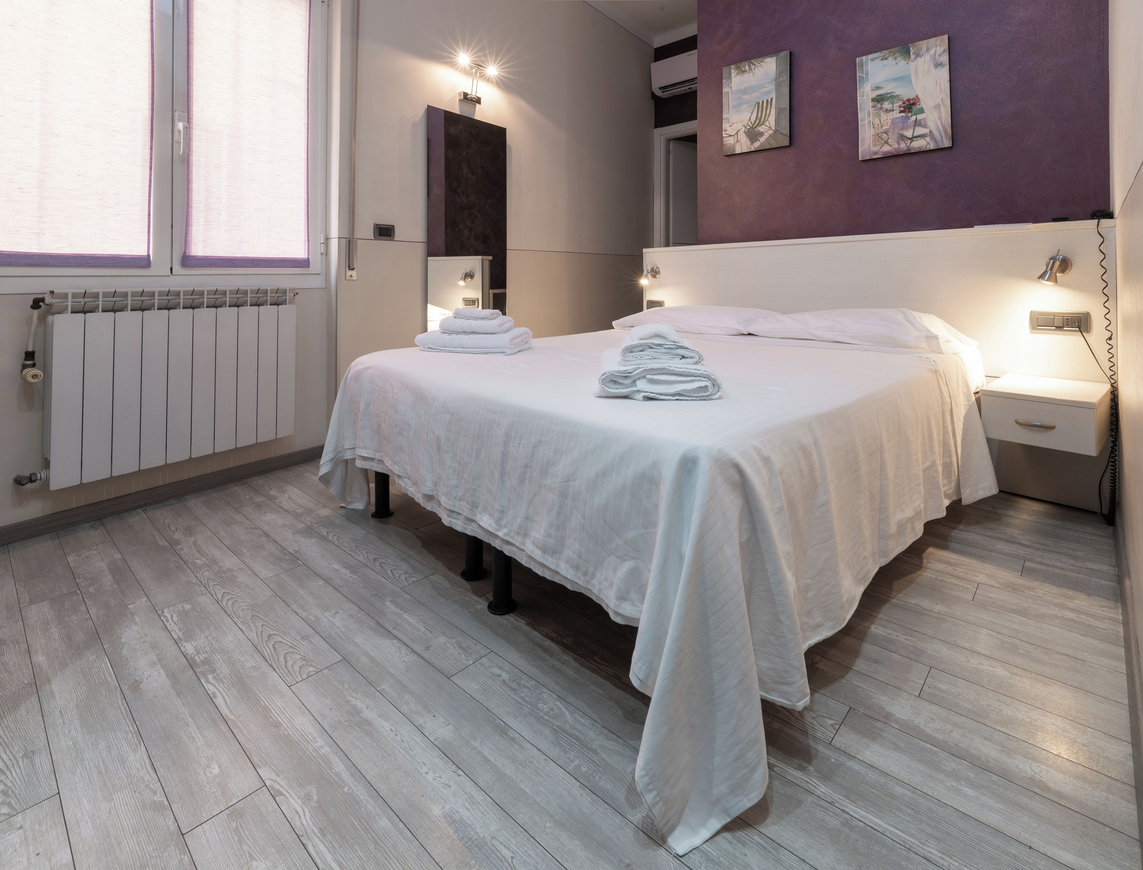 Una camera da letto con un letto, comodini, un termosifone e un'opera d'arte appesa al muro.
