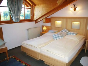 Ein Schlafzimmer mit Holzboden, einem Bett mit weißer Bettwäsche, zwei Nachttischlampen und einem Fenster mit Vorhängen.
