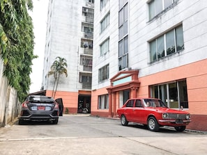 A multi-story building with a red and white facade, a black car parked in front, and a red car parked to the right. - Room-see View Tower Chiang Mai - Good pr (Chiang Mai)