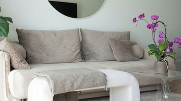 Una sala moderna con un sofá, un espejo redondo, una mesa de centro y una orquídea en maceta.