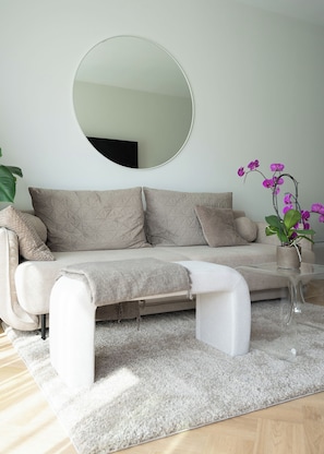 A modern living room with a sofa, a round mirror, a coffee table, and a potted orchid plant. - RentPlanet - Apartament Wilanów (Warszawa)