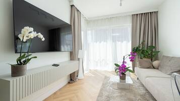 A modern living room with a flat-screen TV, a sofa, a coffee table, and two potted orchids.