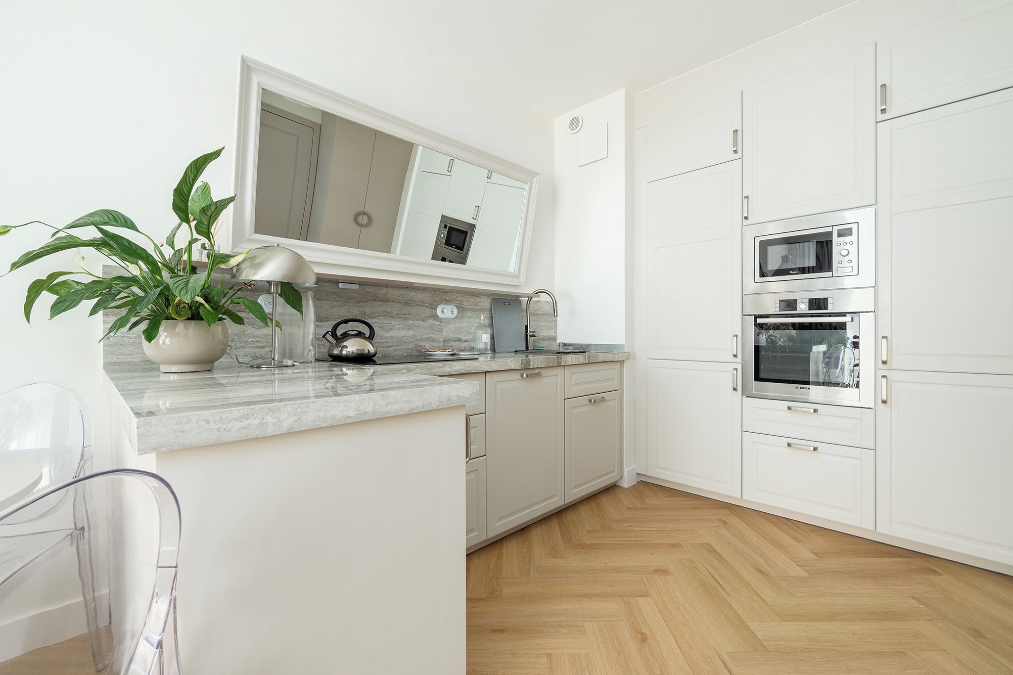 A modern kitchen with white cabinets, a marble countertop, and built-in appliances including a microwave and oven.