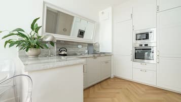 A modern kitchen with white cabinets, a marble countertop, and built-in appliances including a microwave and oven.