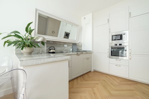 A modern kitchen with white cabinets, a marble countertop, and built-in appliances including a microwave and oven. - RentPlanet - Apartament Wilanów (Warszawa)