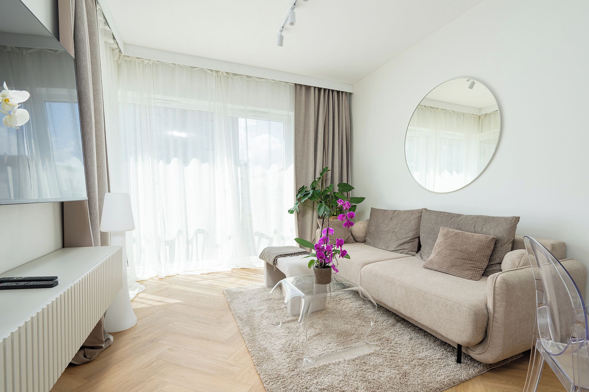 A modern living room with a sofa, a coffee table, a plant, and a round mirror on the wall.