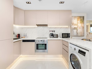 A modern kitchen with built-in appliances, a dishwasher, a microwave, and a washing machine. - Kensington Burj View Studio, Dubai Mall (Dubai)