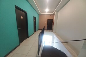 Ein Korridor mit Türen an beiden Seiten sowie einer Treppe in der Mitte und einem Geländer.