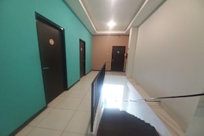 Un pasillo con puertas a ambos lados, una escalera en el centro y una barandilla.