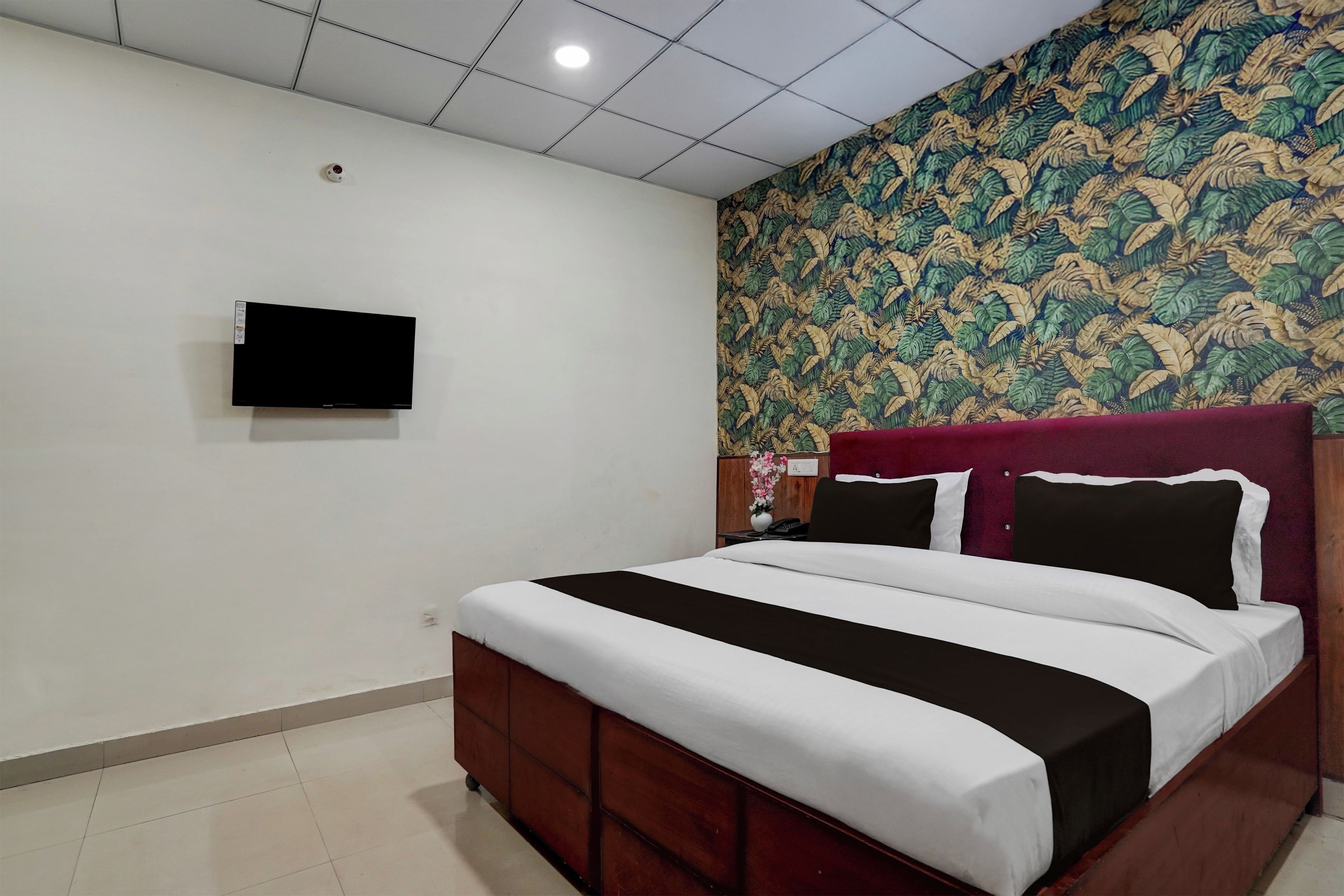 A hotel room with a bed, a television mounted on the wall, and a patterned wallpaper.