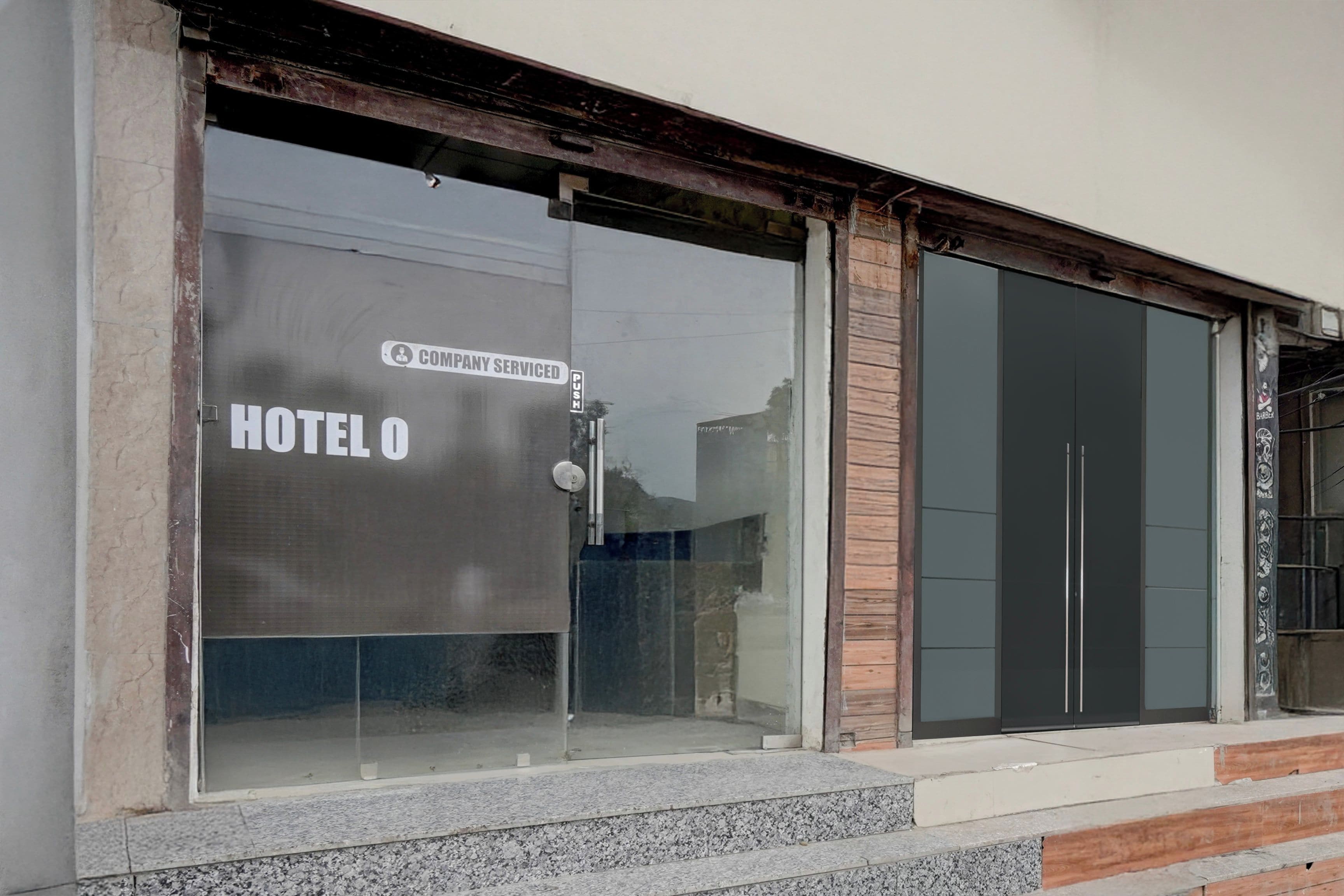 A hotel entrance with a large glass door, a sign indicating it is serviced by a company, and a visible push bar.