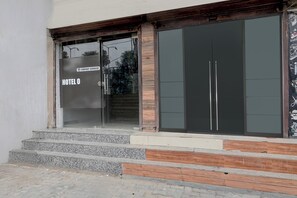 Entrada de un hotel con puerta de vidrio, un cartel que indica que el servicio es proporcionado por una empresa y una escalera que sube hacia la entrada.