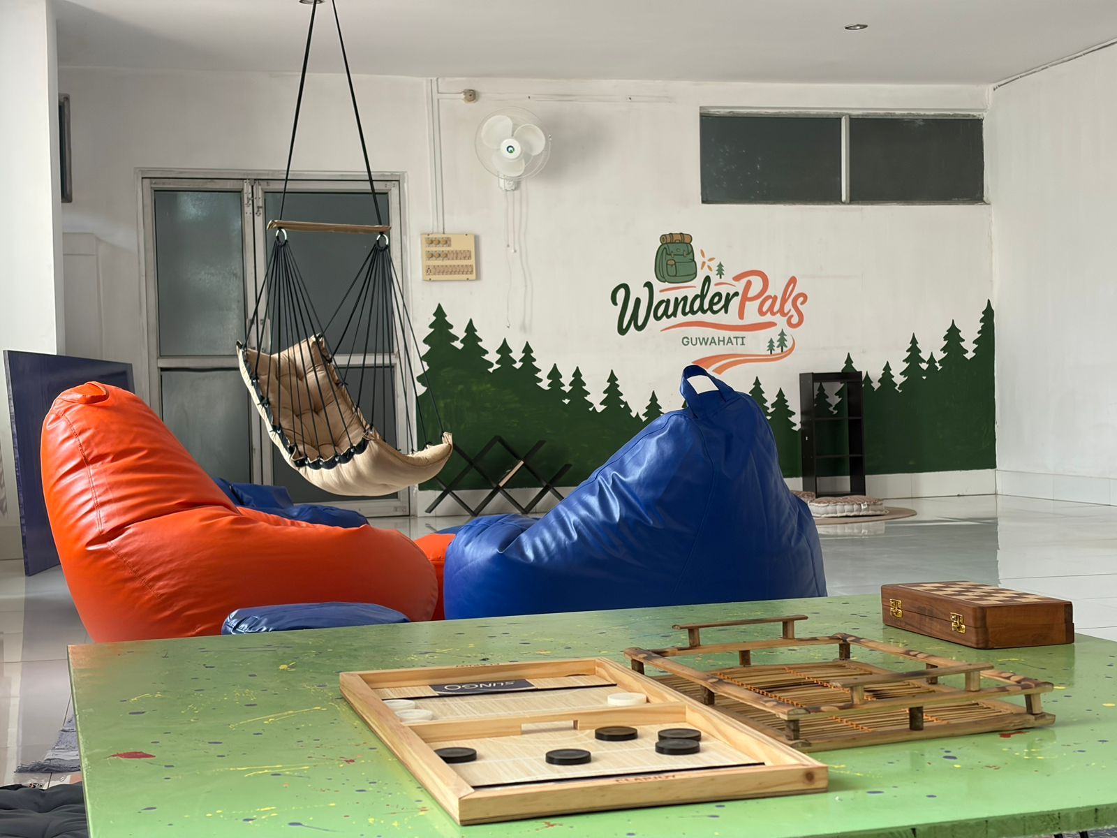 A room with a hammock chair, a wooden board game, and a wall mural.