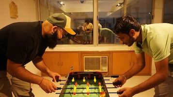 Duas pessoas jogando pebolim em um espaço com armários de madeira e uma janela.