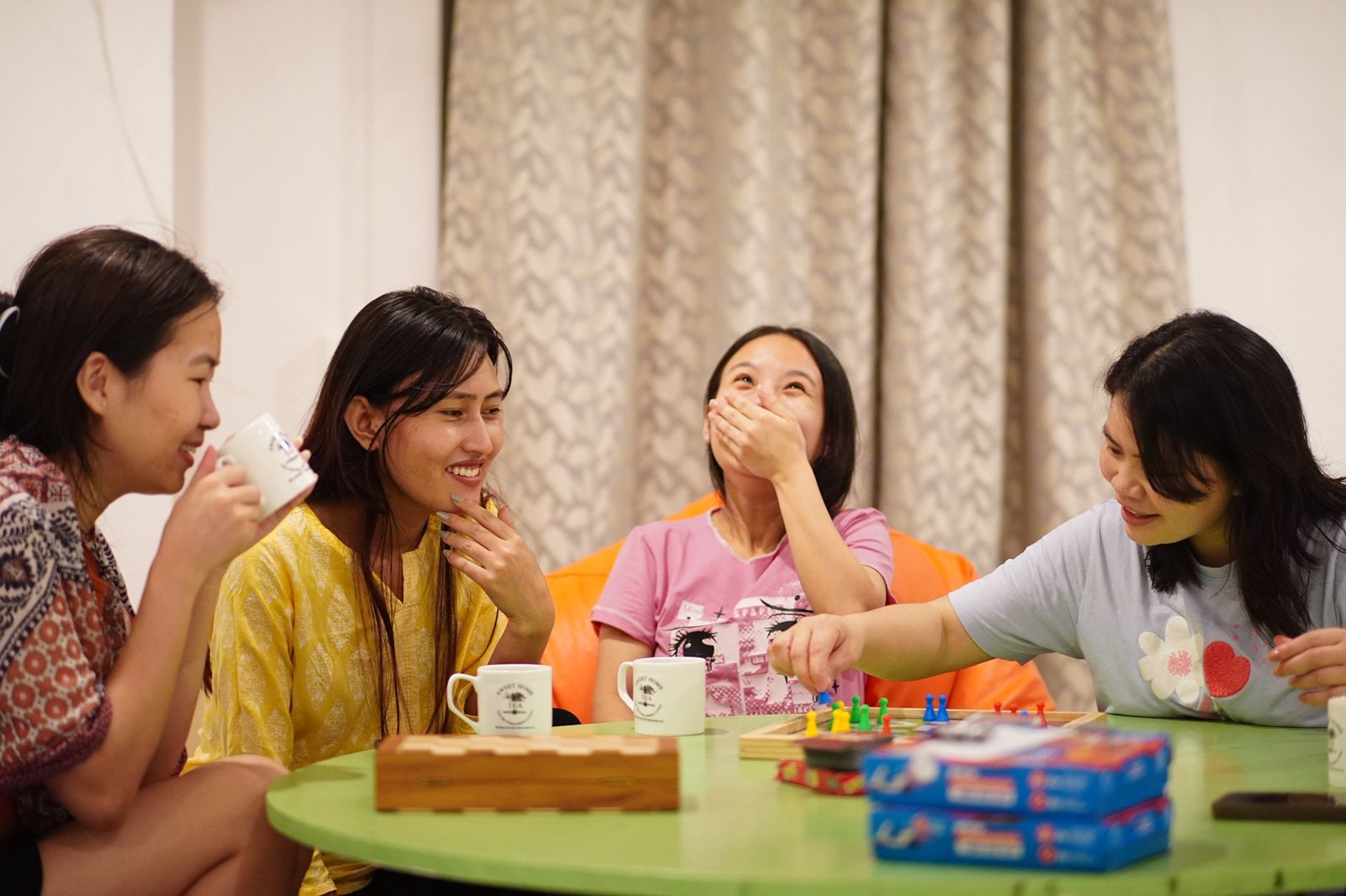 A group of people sitting around a table with a board game, cups, and snacks.
