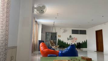 Una habitación con una mesa verde, pufs, una silla colgante y un mural en la pared.