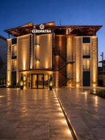 A hotel named 'CLEOPATRA' with a modern architectural design, featuring a prominent entrance with glass doors and a staircase leading to the upper levels.