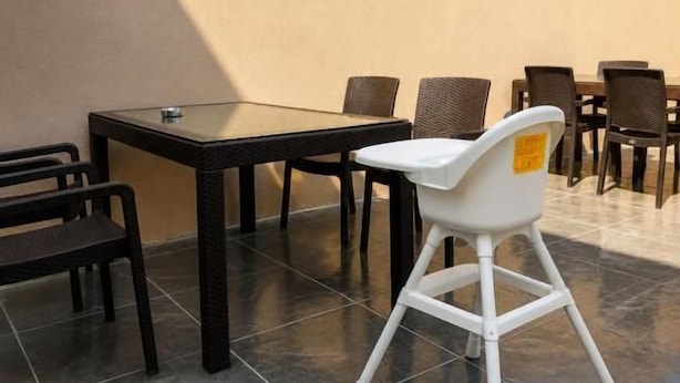 En udendørs terrasse med et bord og stole, en hvid stol samt en beige væg.