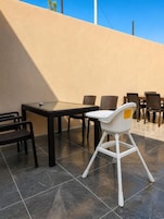 An outdoor patio with a table and chairs, a white chair, and a beige wall.