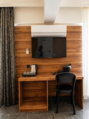 A compact room with a wooden desk, a black chair, a flat-screen TV mounted on the wall, and a coffee maker. - Pamukkale Cleopatra (Pamukkale)