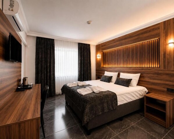 A modern hotel room with a large bed, a flat-screen TV, a wooden panel wall, and a window with curtains. - Pamukkale Cleopatra (Pamukkale)