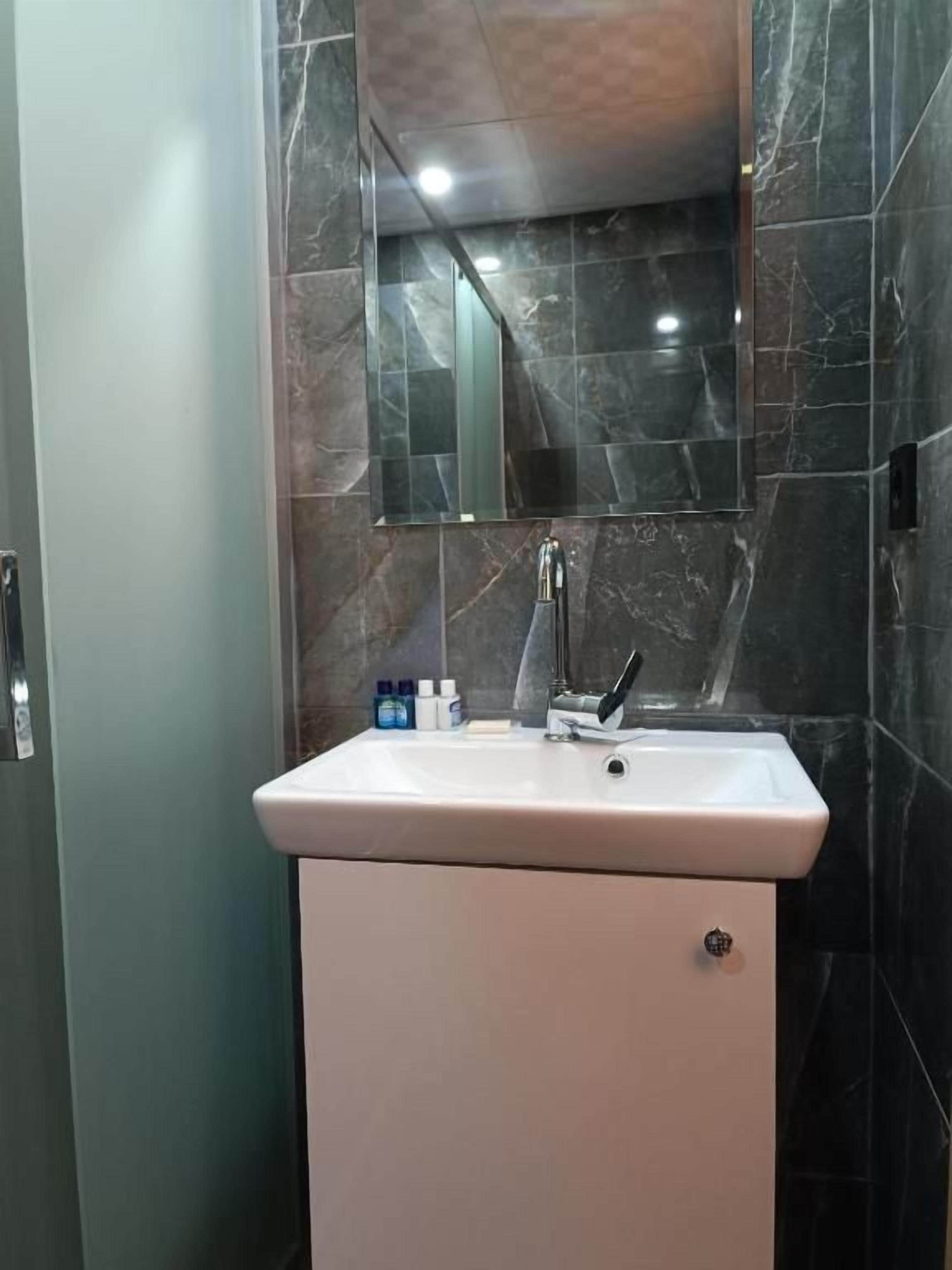 A bathroom with a white sink, a mirror above it, and dark marble walls.