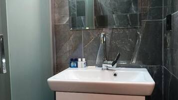 A bathroom with a white sink, a mirror above it, and dark marble walls.