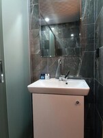 Un baño con lavamanos blanco, un espejo encima y paredes de mármol oscuro.