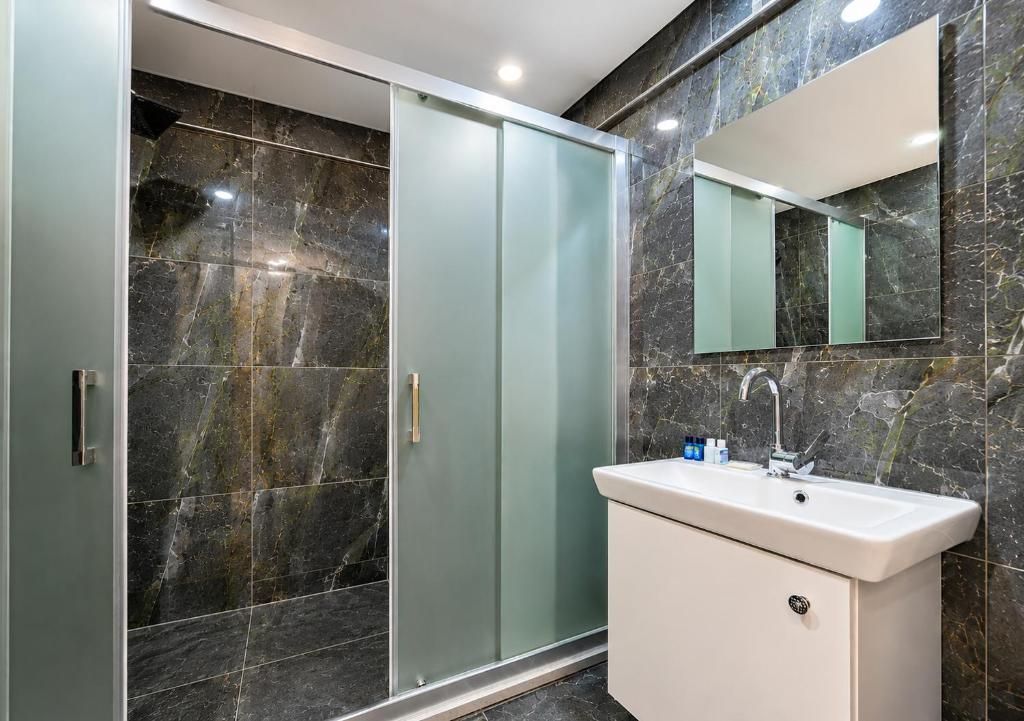 Un baño moderno con cabina de ducha de vidrio, lavabo blanco y pared revestida de mármol.